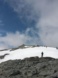 Rear view of man standing on rock against sky during winter