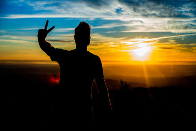 Silhouette man gesturing peace sign against sky during sunset