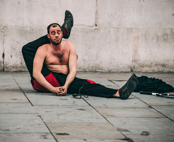 Full length of shirtless man sitting on wall