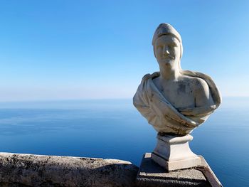 Statue by sea against clear blue sky