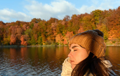 Outdoor portrait of beautiful young woman enjoying sunlight by lake in autumn