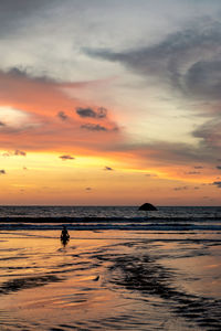 Silhouette person meditating at beach against sky during sunset