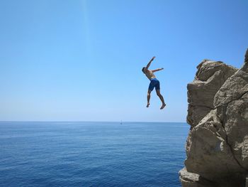 Full length of man jumping in sea against clear blue sky