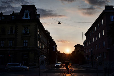 Cars on road amidst buildings against sky during sunset