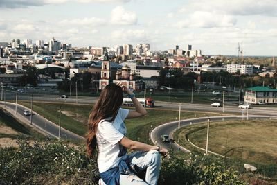 Side view of woman sitting on field against cityscape