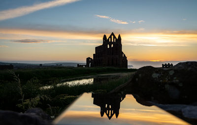 Ancient temple by building against sky during sunset