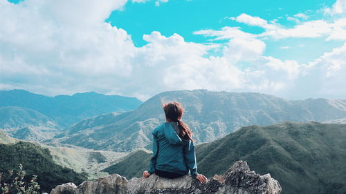 Rear view of woman sitting on rock against mountains during winter