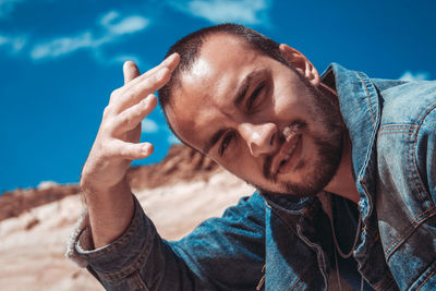 Close-up portrait of young man shielding eyes against sky