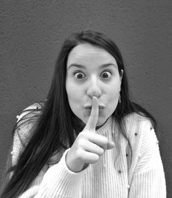 Portrait of beautiful young woman with finger on lips against wall