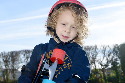 Portrait of cute boy holding skateboard standing against sky