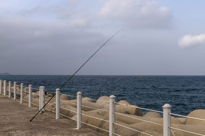 Scenic view of sea with fishing rod against sky