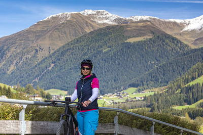 Portrait of woman standing with bicycle by railing against mountains