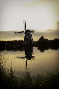 Traditional windmill by lake against sky