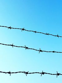 Low angle view of barbed wire against clear blue sky