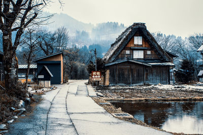 House amidst trees and buildings against sky during winter