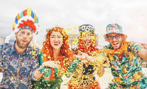 Portrait of happy men and women throwing confetti against sky