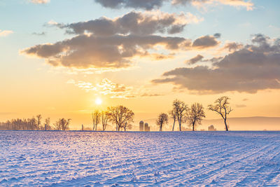 Snow covered field against sky during sunset