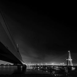 Illuminated bridge over river against sky in city at night