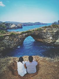 Rear view of couple sitting by sea against sky