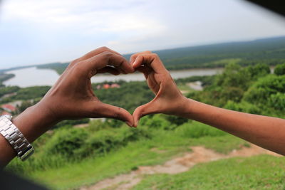 Cropped hands of couple making heart shape against landscape