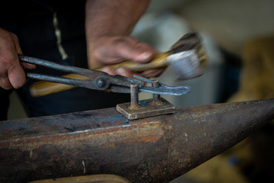 Midsection of man hammering horseshoe on anvil in workshop