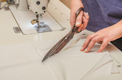 Dressmaker cuts white cloth with large knives.