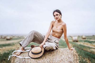 Young woman wearing hat sitting on field against sky