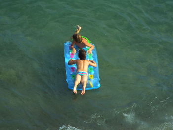 High angle view of shirtless friends on inflatable floating on sea