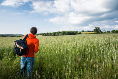 Rear view of backpack man standing on wheat field against cloudy sky