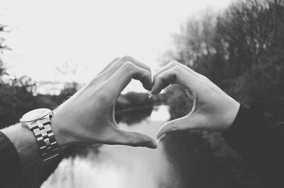 Cropped hands of couple making heart shape over river