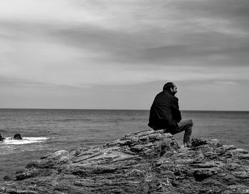Man on rock at beach against sky