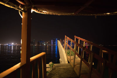 Illuminated pier over sea against sky at night