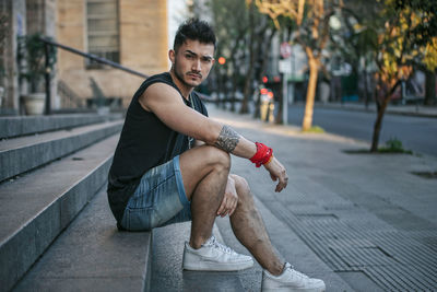 Portrait of young man sitting on footpath