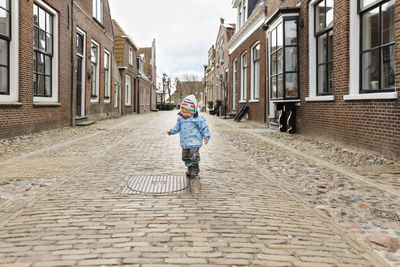 Full length of girl wearing warm clothing walking on street amidst buildings