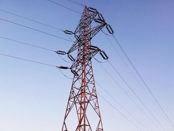 Low angle view of electricity pylon against clear blue sky