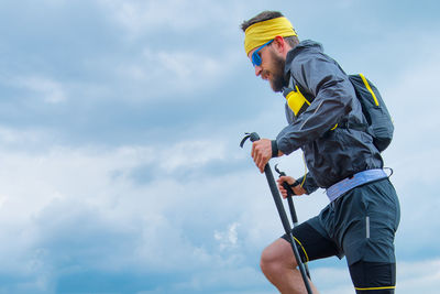 Man practicing trail running with sticks in the mountains with the sky background