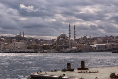 Sea by mosques in city against cloudy sky