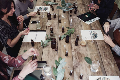 High angle view of multi-ethnic female colleagues preparing perfume at table in workshop