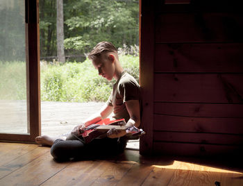 Side view of teenage boy playing guitar while sitting at doorway
