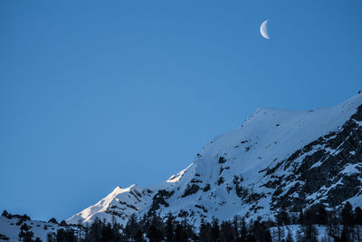 Low angle view of snowcapped mountains against clear blue sky