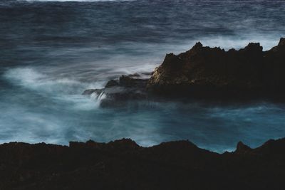 Scenic view of sea by silhouette mountain against sky