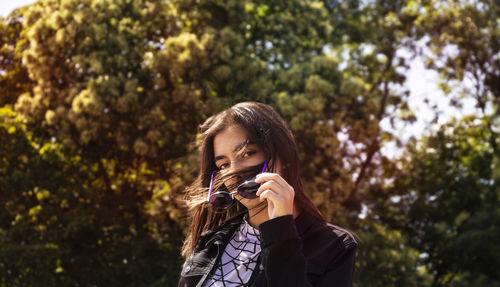 Portrait of young woman photographing against trees