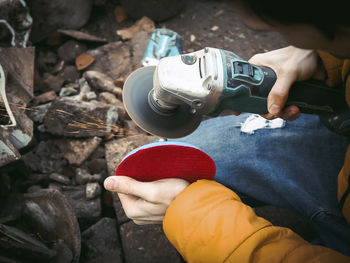 The hands of a young caucasian man in a yellow jacket are holding a drill and polishing with a disc