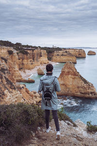 Rear view of man standing on rock against sky