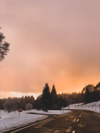 Snow covered field against sky during sunset