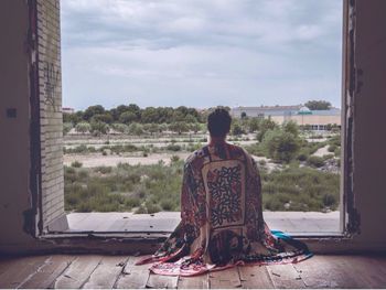 Rear view of woman sitting on window