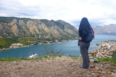 Woman standing on mountain by lake against sky