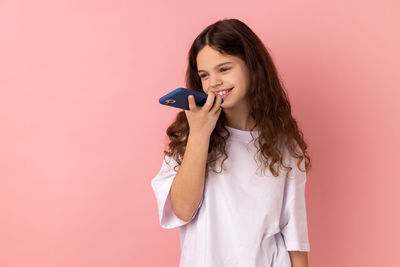 Young woman talking on mobile phone against pink background