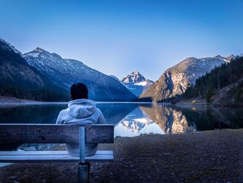 Rear view of man sitting on snowcapped mountains against clear sky