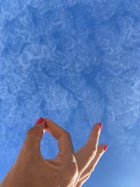 Close-up of hand against blue sky